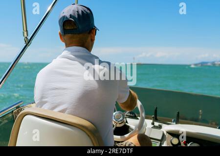 Vue de Bach d'un homme d'âge moyen conduisant un yacht à moteur de luxe. Capitaine à la barre du bateau à moteur. Image avec mise au point sélective Banque D'Images