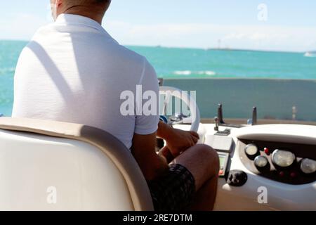 Vue de Bach d'un homme d'âge moyen conduisant un yacht à moteur de luxe. Capitaine à la barre du bateau à moteur. Image avec mise au point sélective Banque D'Images