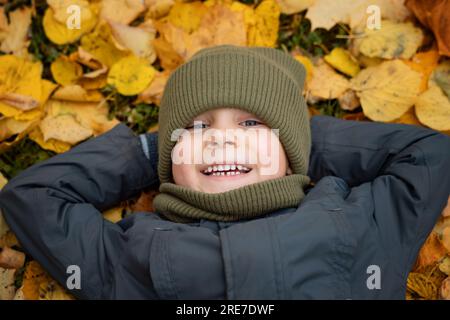 mignon petit garçon allongé sur le sol recouvert de feuilles jaunes tombées. Photo de haute qualité Banque D'Images