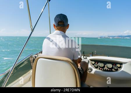 Vue de Bach d'un homme d'âge moyen conduisant un yacht à moteur de luxe. Capitaine à la barre du bateau à moteur. Image avec mise au point sélective Banque D'Images