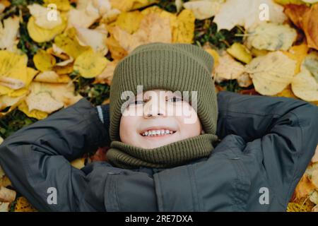 mignon petit garçon allongé sur le sol recouvert de feuilles jaunes tombées. Photo de haute qualité Banque D'Images