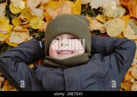 mignon petit garçon allongé sur le sol recouvert de feuilles jaunes tombées. Photo de haute qualité Banque D'Images