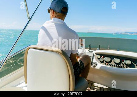 Vue de Bach d'un homme d'âge moyen conduisant un yacht à moteur de luxe. Capitaine à la barre du bateau à moteur. Image avec mise au point sélective Banque D'Images