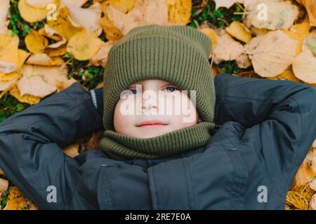 mignon petit garçon allongé sur le sol recouvert de feuilles jaunes tombées. Photo de haute qualité Banque D'Images