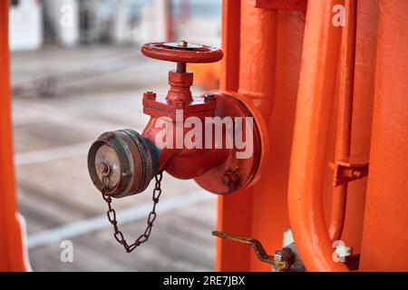 Vanne d'isolement du collecteur d'incendie pour navire offshore de couleur rouge fixée au tuyau orange. Banque D'Images