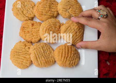 Thekua , un plat indien sucré snacks dans une assiette blanche . main de femme mettant thekua sur l'assiette. Populaire à bihar jharkhand. Prashad in chhath maha parv. Banque D'Images