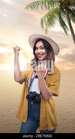 Femme asiatique avec un chapeau et une caméra avec une expression excitée dans le fond de scène de coucher de soleil Banque D'Images