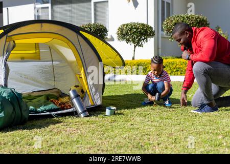 Heureux fils afro-américains et père lançant tente ensemble dans le jardin ensoleillé, espace de copie Banque D'Images