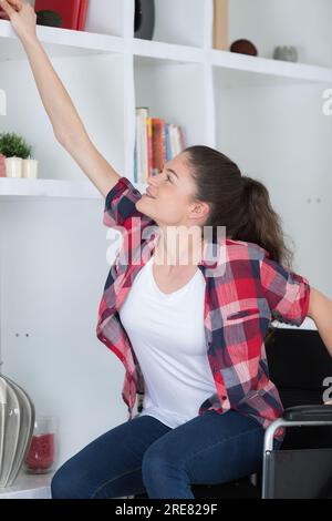 femme en fauteuil roulant atteignant pour quelque chose de l'étagère du salon Banque D'Images