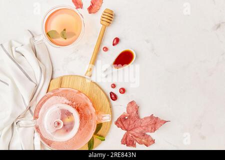 Table d'automne esthétique avec théière en verre et tasse de thé aux baies naturelles parmi les feuilles. Espace de copie. Banque D'Images