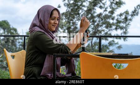 Portrait d'une jeune femme musulmane utilisant un téléphone portable dans un café en plein air Banque D'Images