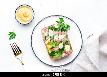 Viande aspic d'hiver, bœuf bouilli froid dans un bouillon de gelée épicé sur assiette avec ail et vinaigrette à la moutarde de dijon. Fond de table blanc, vue de dessus Banque D'Images