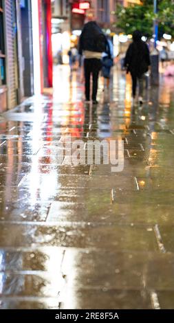 Des gens se réfugiant de la pluie la nuit dans une rue de Londres sous un abri de bus. Banque D'Images