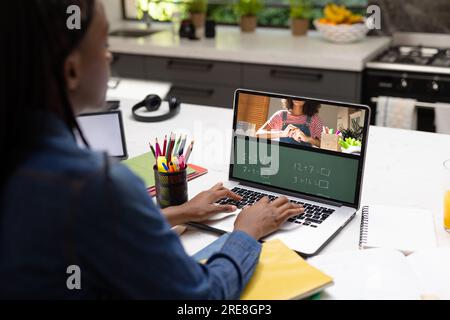 Vue arrière d'une écolière afro-américaine ayant un appel vidéo avec une enseignante sur ordinateur portable Banque D'Images