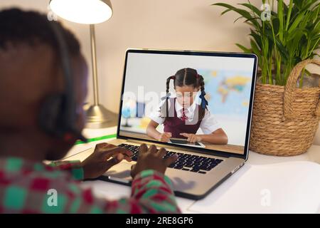 Vue arrière d'un garçon afro-américain utilisant un ordinateur portable tout en ayant un appel vidéo avec une fille biracial Banque D'Images