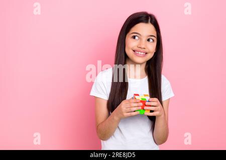 Portrait photo d'adorable écolière femme look espace vide rubik cube habillé de vêtements blancs élégants isolé sur fond de couleur rose Banque D'Images