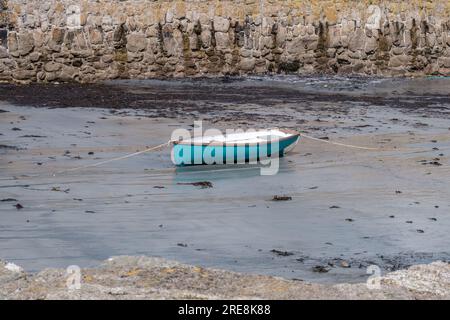 Un bateau en rangée est échouée à marée basse avec un ancien mur de pierre en arrière-plan au port de St Michael’s Mount, Marazion, Cornouailles, Angleterre. Banque D'Images