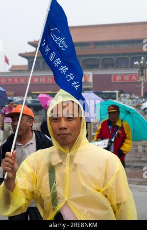 Guide touristique chinois portant des vêtements de pluie conduit un groupe de touristes équipés de parapluies sur une journée humide sur la place Tiananmen, Pékin, Chine. Portrait du président Mao Tse Tung montres depuis les murs de la Cité interdite. (125) Banque D'Images
