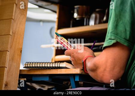 Homme dessinant sur un cahier et tenant des crayons sur une table dans un van converti Banque D'Images