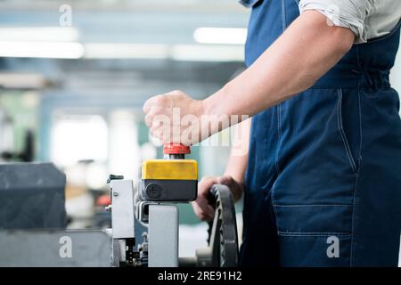 Gros plan d'un ouvrier d'usine méconnaissable dans une machine industrielle fonctionnant avec télécommande, il appuie sur le bouton ed tout en lançant le convoyeur Banque D'Images