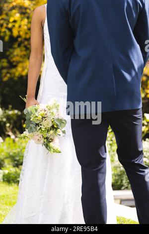 Section médiane de mariée afro-américaine avec bouquet et marié debout dans le jardin ensoleillé Banque D'Images