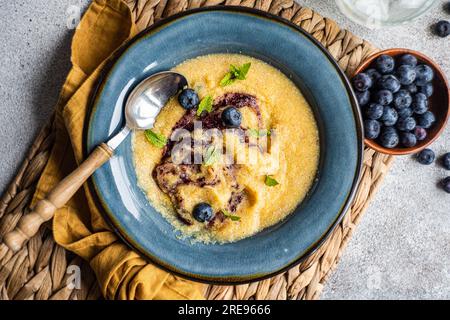 Vue de dessus de la bouillie de polenta avec de la menthe et de la confiture près des myrtilles fraîches dans un bol sur la table Banque D'Images