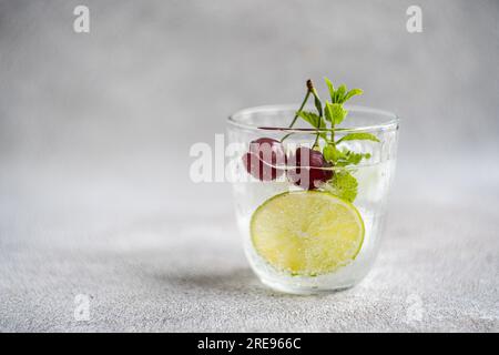 Verre transparent de boisson fraîche rafraîchissante avec des feuilles de citron vert et de menthe sur la surface grise dans la journée d'été sur fond flou Banque D'Images