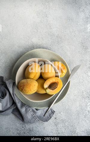 Vue de dessus du bol en céramique avec des abricots jaunes mûrs frais placés sur un tissu bleu sur une table en béton avec coupe en demi abricot Banque D'Images