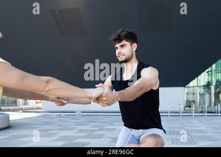Souriant jeune homme fort avec une femme anonyme se regardant tout en se tenant debout avec la jambe pliée et tenant les mains avec les bras tendus en plein jour Banque D'Images