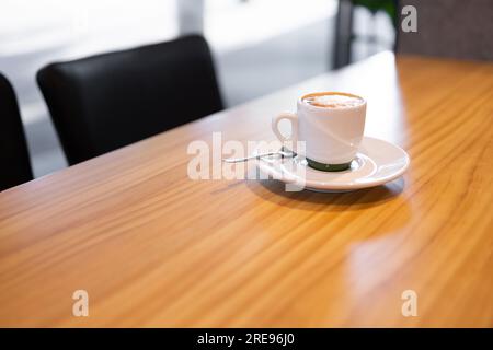Angle élevé de tasse en céramique blanche avec cappuccino placé sur la table en bois dans la salle de bureau Banque D'Images