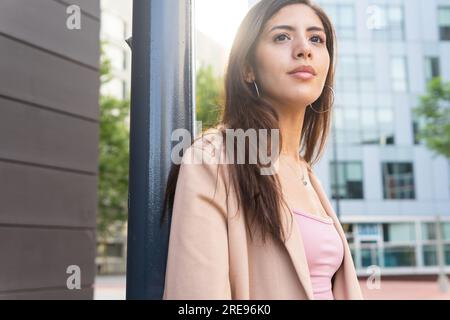 D'en bas de pensive hispanique femme entrepreneur dans des vêtements formels debout près du bâtiment regardant loin Banque D'Images