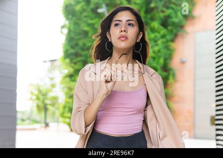 Pensive yo jeune femme entrepreneure hispanique marchant dans la rue urbaine et tenant des lunettes Banque D'Images