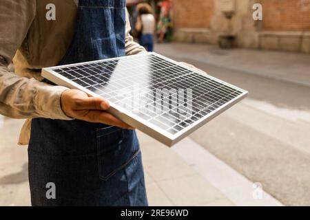 Homme recadré méconnaissable dans des vêtements décontractés debout sur la rue tenant le panneau solaire portable à la lumière du jour Banque D'Images