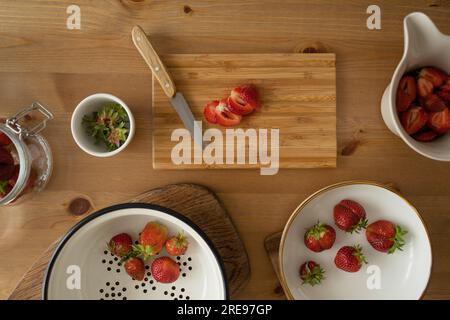 Du dessus des fraises fraîchement tranchées sur une planche de bois et dans un bol avec couteau placé sur une table en bois pendant la préparation de confiture de fraises à l'intérieur Banque D'Images