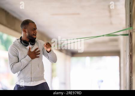 Vue latérale d'un jeune homme barbu afro-américain concentré en vêtements de sport regardant loin tout en se tenant debout et en s'exerçant avec la main sur la poitrine avec résistance b Banque D'Images