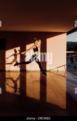 Jeune femme sportive de race blanche travaillant au coucher du soleil pratiquant des sauts, des ombres et de la lumière sur fond Banque D'Images