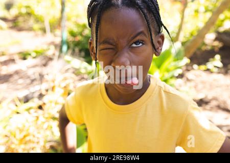 Garçon afro-américain portant un t-shirt jaune, faisant un visage drôle dans le jardin Banque D'Images