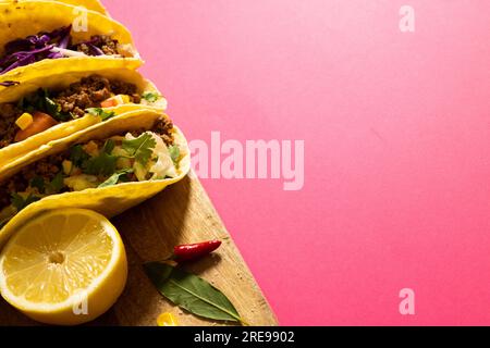 Vue à grand angle des tacos garnis de tranches de citron, de piment rouge et de feuilles sur la planche de service, espace de copie Banque D'Images