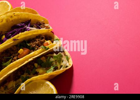 Vue à angle élevé des tacos avec des tranches de citron sur fond rose, espace de copie Banque D'Images