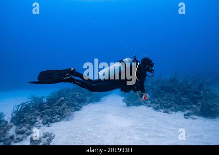 Vue latérale du plongeur nageant sous l'eau avec des bulles tout en explorant la mer claire profonde pendant la visite de plongée à Cancun Banque D'Images