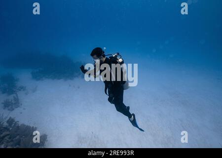 Vue latérale du plongeur nageant sous l'eau avec des bulles et regardant vers le bas tout en explorant la mer claire profonde pendant la visite de plongée à Cancun Banque D'Images