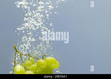 Gros plan de raisins blancs tombant dans l'eau avec espace de copie sur fond gris Banque D'Images