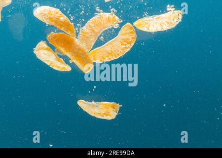 Gros plan de segments de mandarine tombant dans l'eau avec espace de copie sur fond bleu Banque D'Images