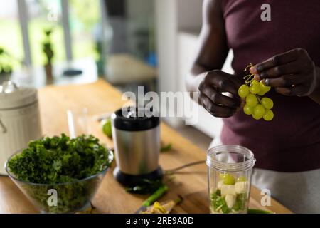 Section médiane de l'homme afro-américain préparant un smoothie sain dans la cuisine à la maison Banque D'Images