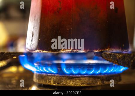 Gros plan de pot moka rouge avec infusion de café sur cuisinière à gaz butane incandescente dans la cuisine Banque D'Images