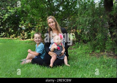 Mère et ses deux enfants profitent d'une belle journée en plein air. Ils sont assis sur l'herbe. Mère tient le bébé et le fils est assis près d'elle Banque D'Images