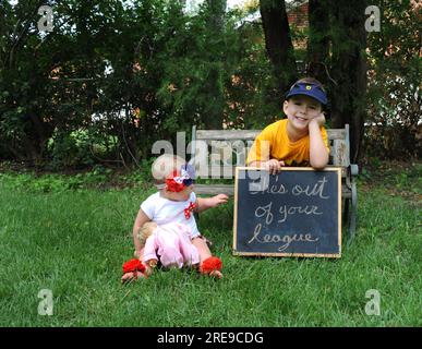 Sœur semble pointer le signe qui avertit le grand frère qu'elle est «hors de sa ligue». Frère est penché sur signe souriant. Banque D'Images