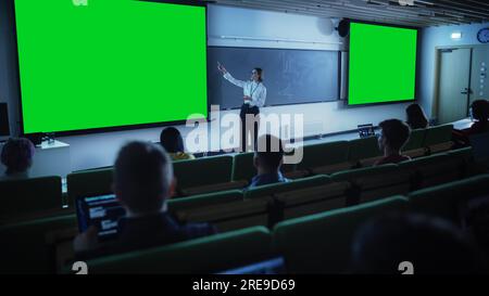 Jeune professeur d'université féminin expliquant une conférence, pointant sur un écran vert Mock Up Display. Groupe de divers étudiants multiethniques Banque D'Images