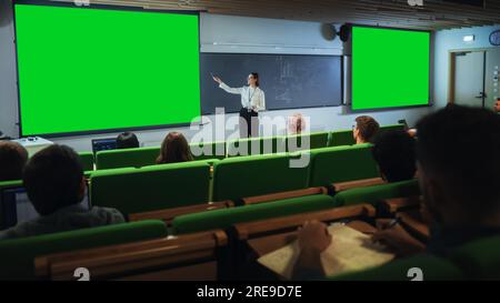 Jeune professeur d'université féminin expliquant une conférence, pointant sur un écran vert Mock Up Display. Groupe de divers étudiants multiethniques Banque D'Images