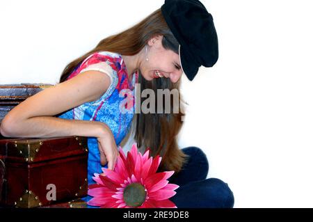 Adolescente se fait renverser sa boîte à chatouilles, et rit hillarieusement. Elle est appuyée sur un ensemble de vieilles valises et tient une Marguerite rose chaude. Banque D'Images